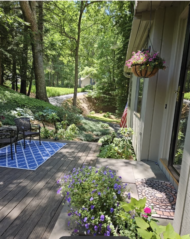 Sunlit back deck surrounded by woods and flowers